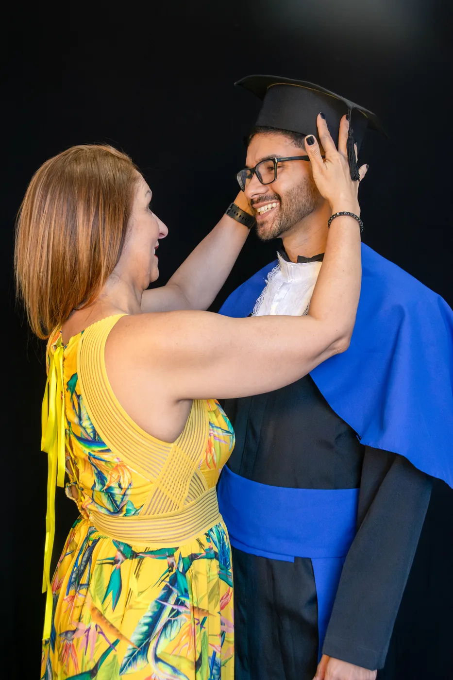 Mãe ajeitando o capelo do formando, momento emocionado em estúdio com fundo preto