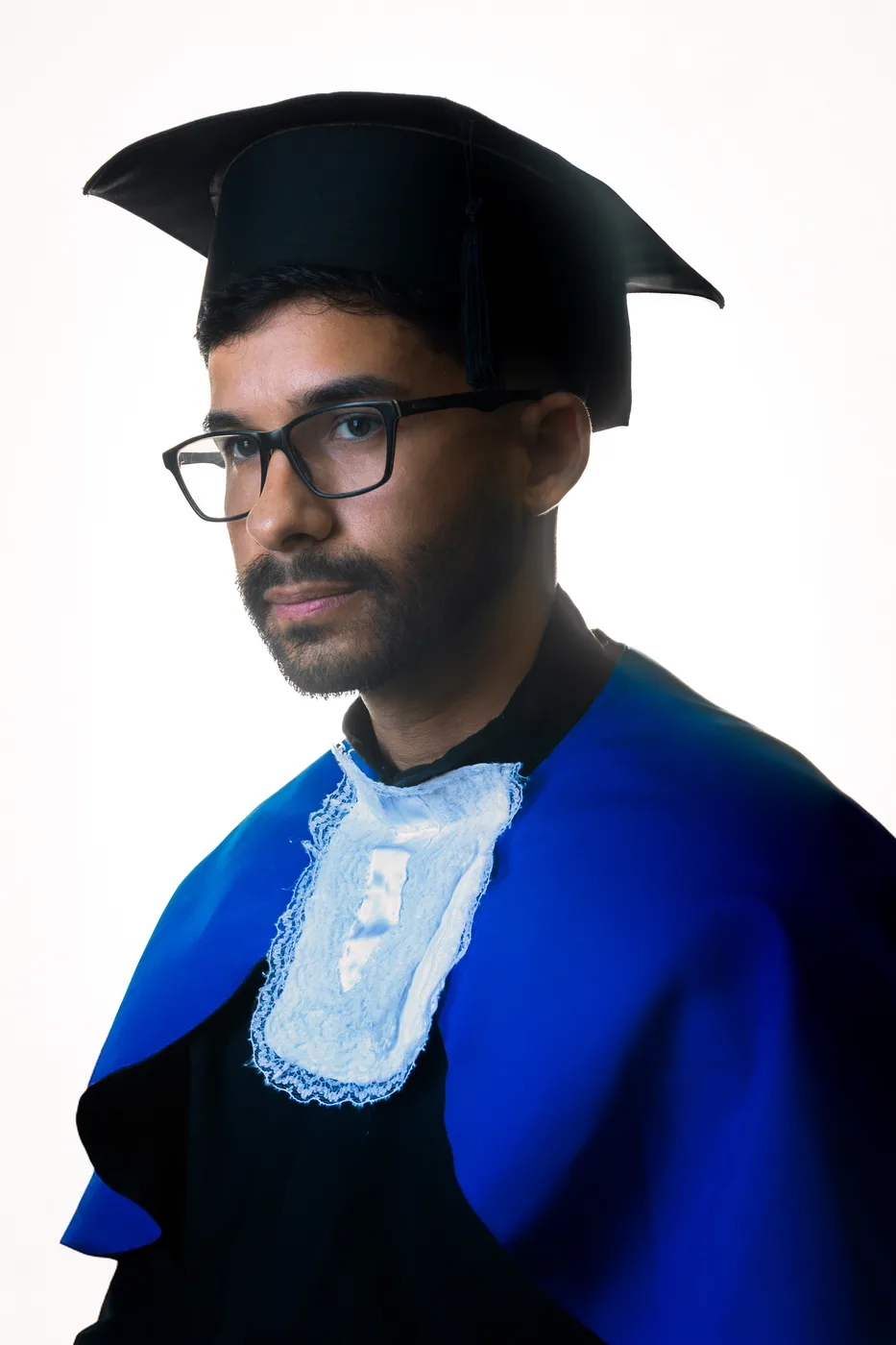 Formando de beca e capelo em retrato de perfil, luz dramática, fundo branco em estúdio